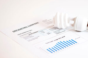 An energy-efficient lightbulb laying on a monthly energy bill that has been lowered due to air duct cleaning services in Springfield, IL.