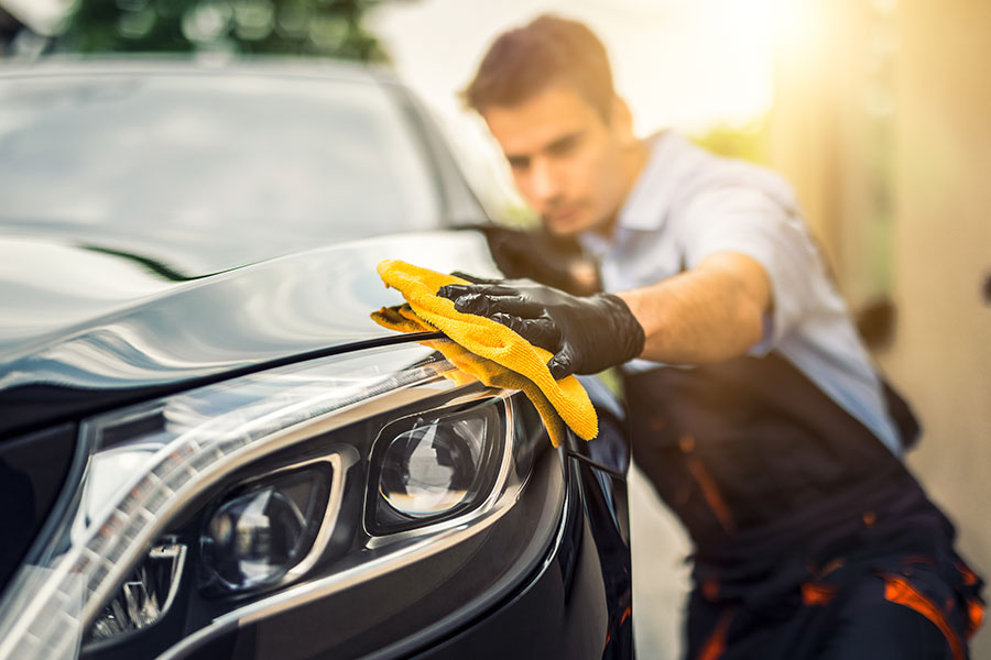 A car detailing expert in Springfield, IL using a yellow rag to clean and detail the exterior of a vehicle for a client.